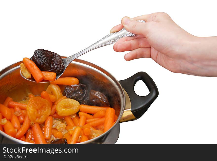 A hand taking off the stewed baby carrots with dried fruits from the pan isolated on white