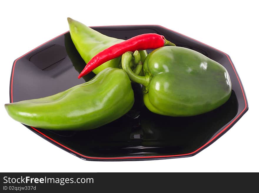 Three green peppers and red chili on the black plate isolated on white