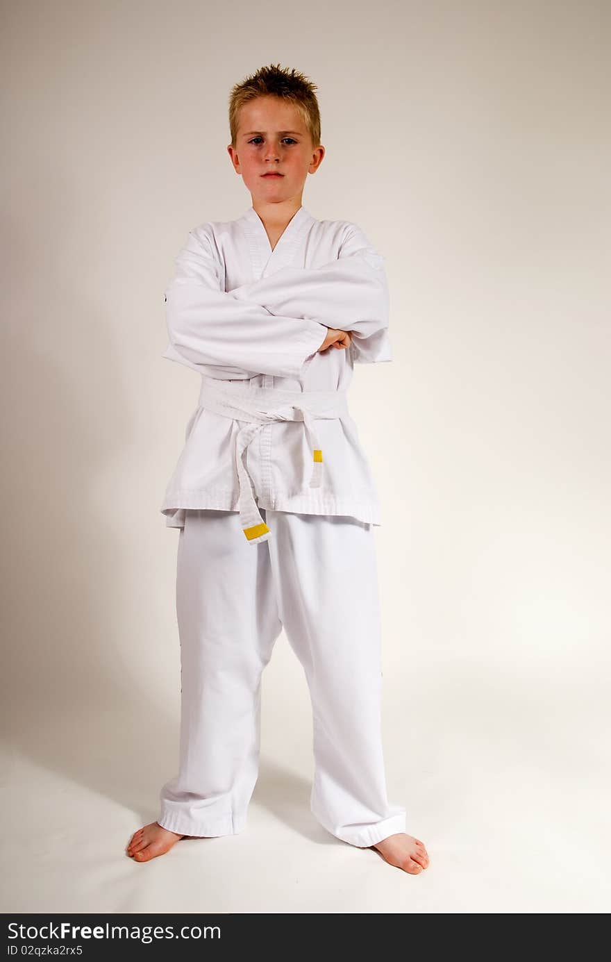 A vertical image of a young teenage boy in karate suit standing with arms folded and a serious look on his face, isolated against a plain background. A vertical image of a young teenage boy in karate suit standing with arms folded and a serious look on his face, isolated against a plain background