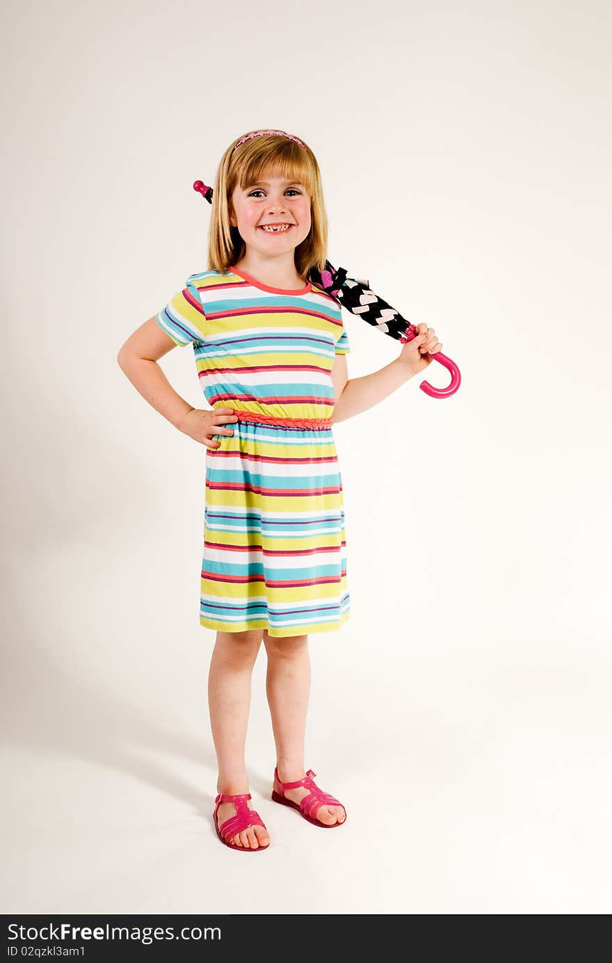 A vertical image of a lovely and cute little girl standing in her sundress and sandles with a rolled up umbrella over her sholder and a lovely smile isolated against a plain background. A vertical image of a lovely and cute little girl standing in her sundress and sandles with a rolled up umbrella over her sholder and a lovely smile isolated against a plain background