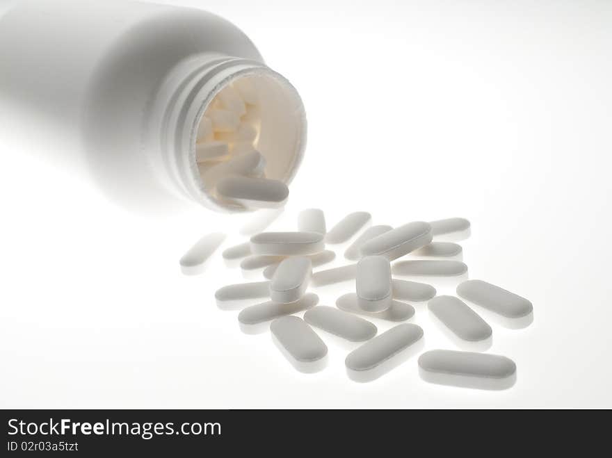 Close up of prescription medicine pills pouring out of white bottle on white background. Close up of prescription medicine pills pouring out of white bottle on white background