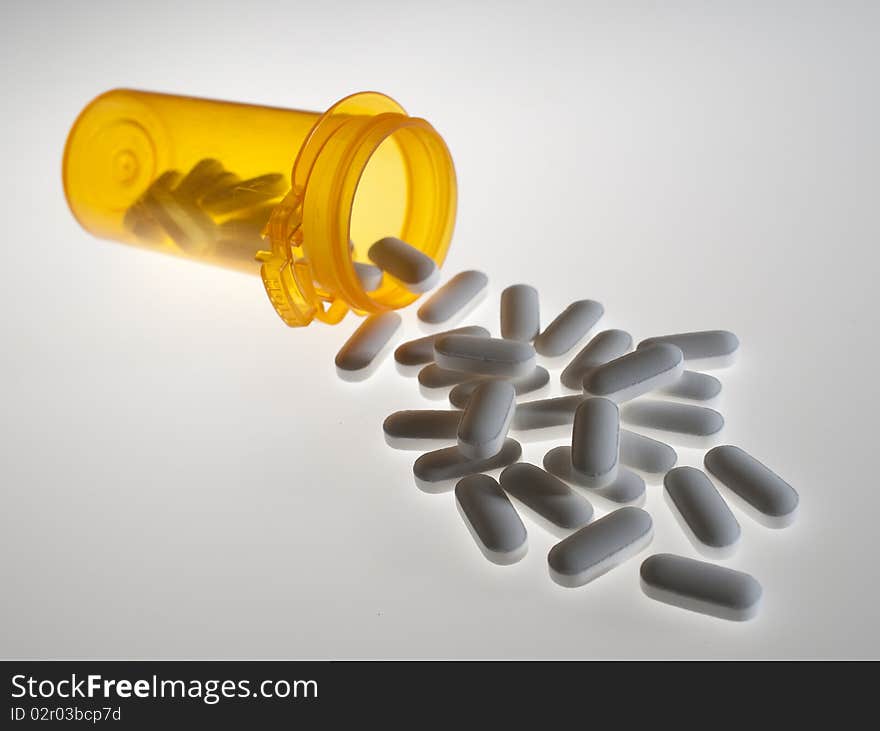 Close up of prescription medicine pills pouring out of orange bottle on white background. Close up of prescription medicine pills pouring out of orange bottle on white background