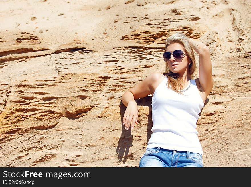 Young girl the blonde in jeans, against sand