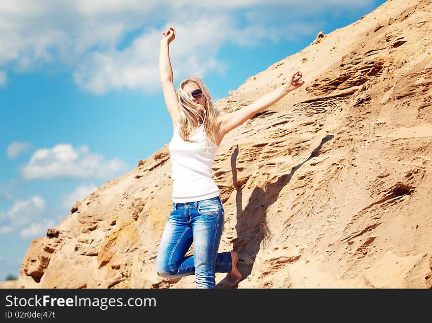 Young girl the blonde in jeans, against sand