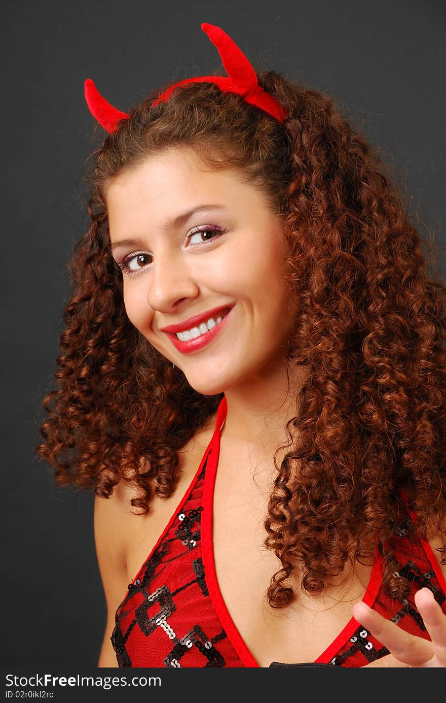 woman is smiling broadly and looking at the camera. Small red horns are in her curly hair. woman is smiling broadly and looking at the camera. Small red horns are in her curly hair