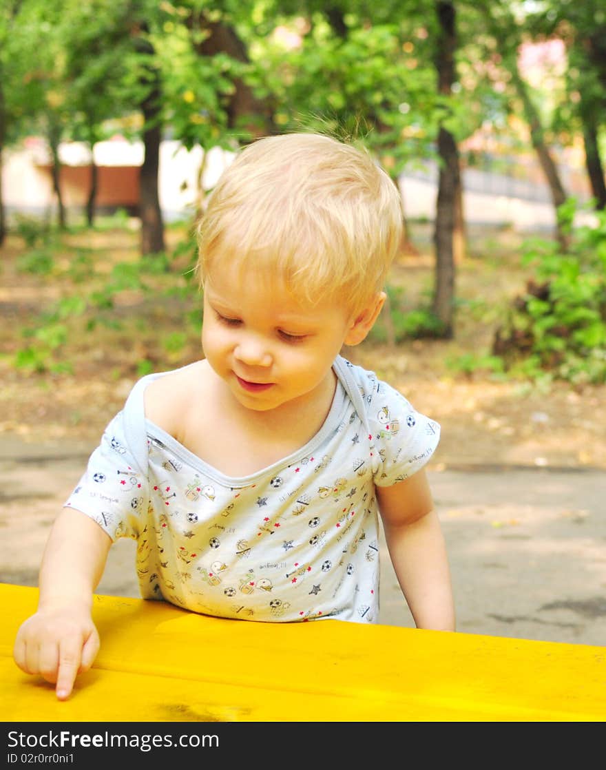 Little handsome boy draws a finger on the yellow bench. Little handsome boy draws a finger on the yellow bench