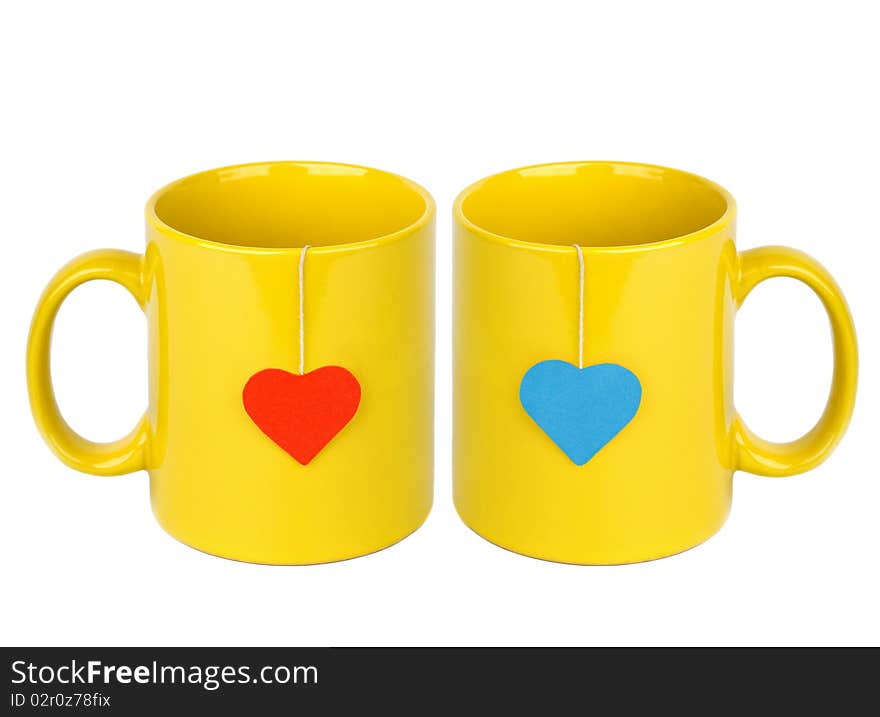 Tea bags with red and blue heart-shaped lables in yellow cups isolated on white. Tea for two. Tea bags with red and blue heart-shaped lables in yellow cups isolated on white. Tea for two