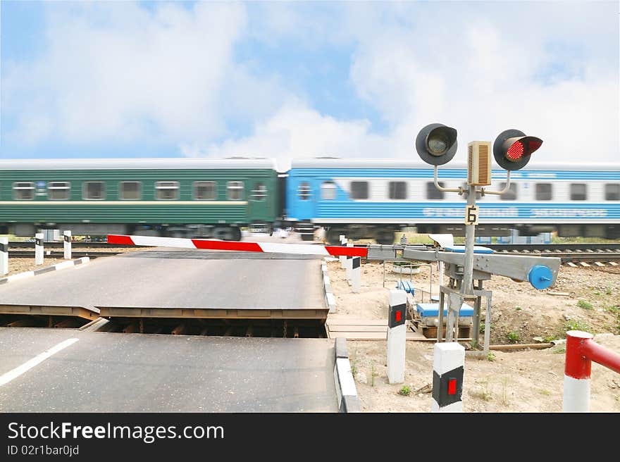 The image of railway crossing and the train. Focus is under the traffic light. Train us blurred.