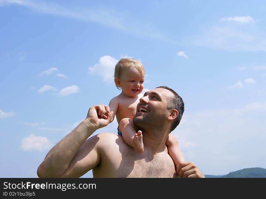 In the summer against the sky the man holds the baby for hands having put to itself on shoulders. In the summer against the sky the man holds the baby for hands having put to itself on shoulders