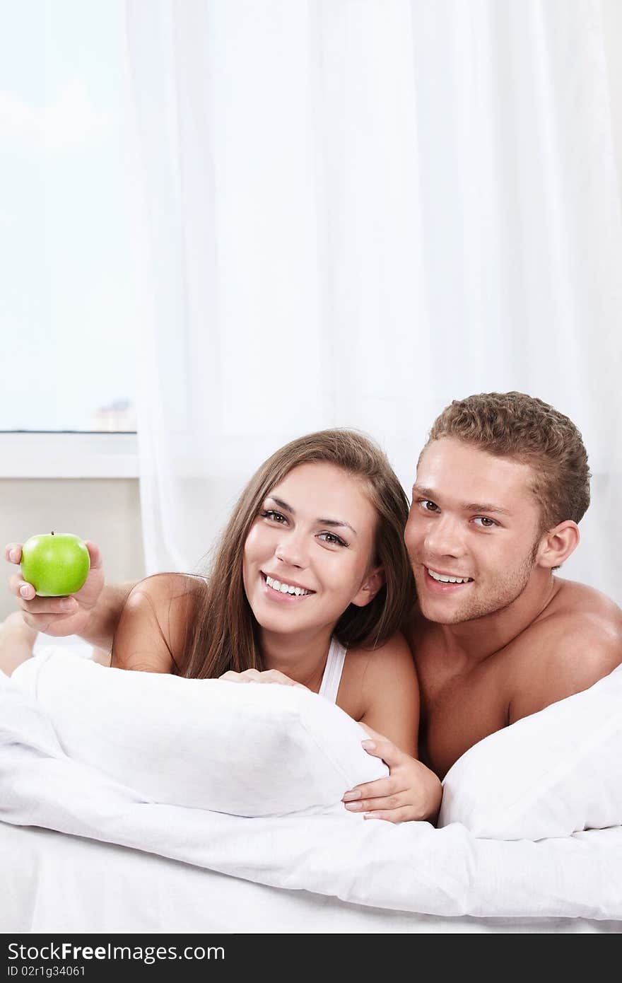 Young happy couple in bed with apple. Young happy couple in bed with apple