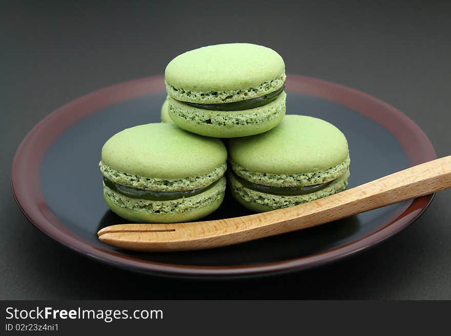 French green tea Macarons served on a black and brown plate with a wooden fork on black background. French green tea Macarons served on a black and brown plate with a wooden fork on black background.