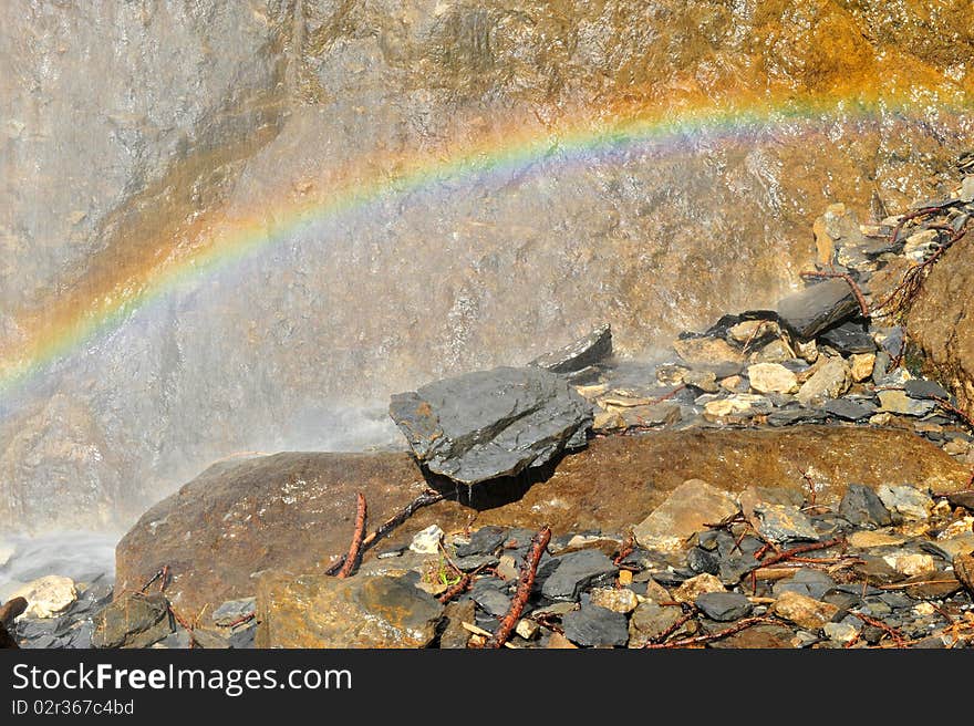 Rainbow over rocks under a small waterfall.