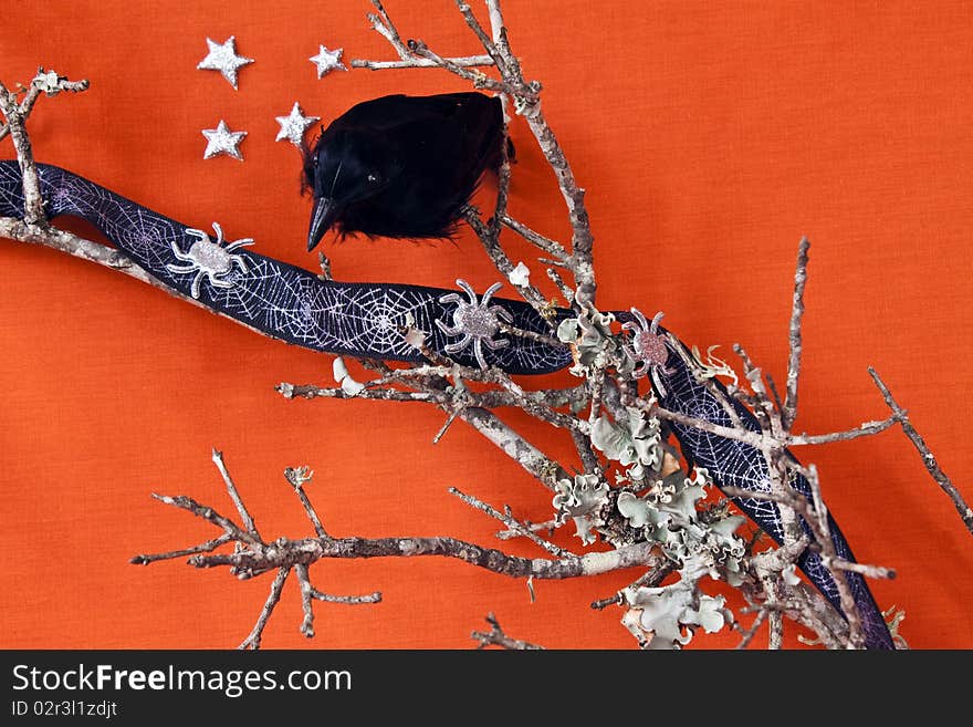 Halloween Raven on a dead branch with spiders and stars on an orange textile