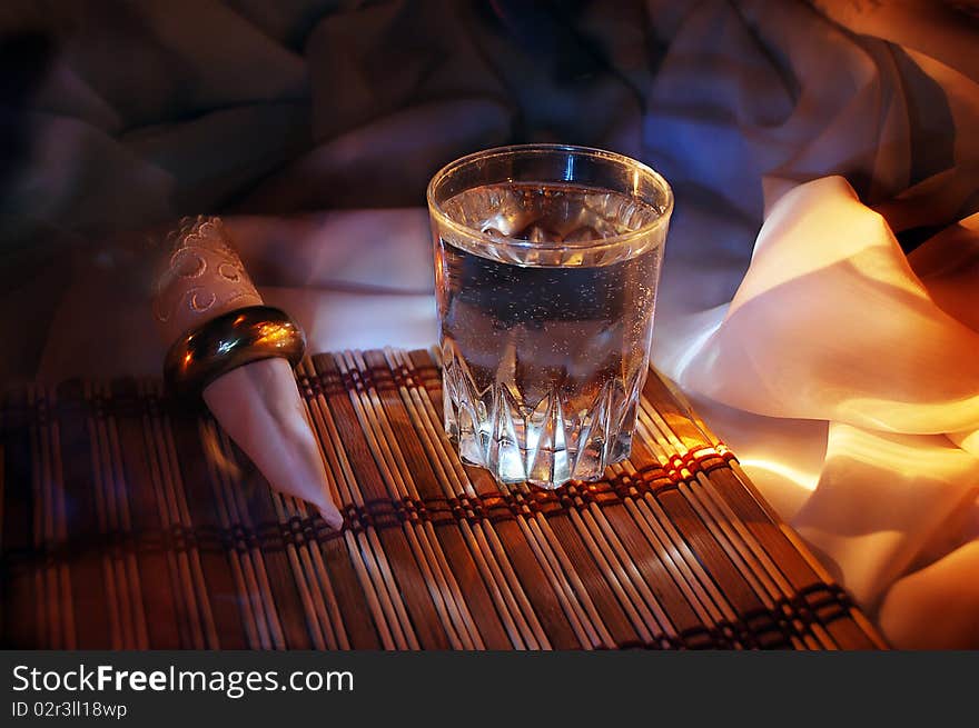 Glass, standing on a mat, alongside convolute serviette, warm light, comfort of little cafe. Glass, standing on a mat, alongside convolute serviette, warm light, comfort of little cafe