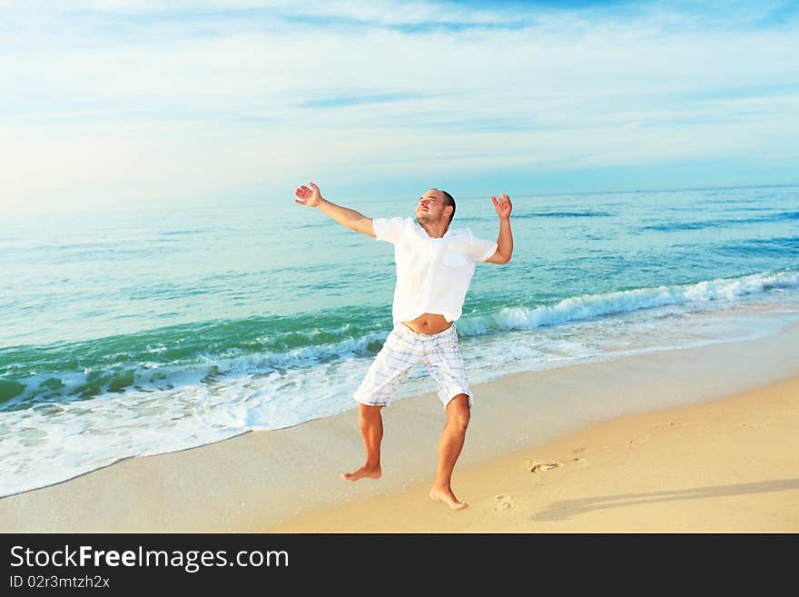 Happy man jumping on the beach at sunrise