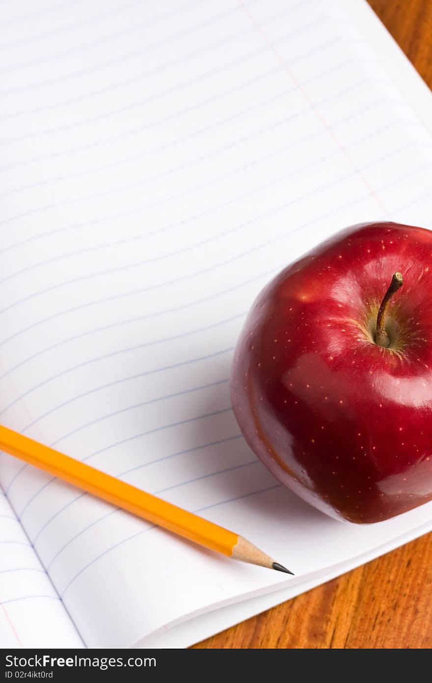 A red apple and pencil sitting on an opened notebook.  Concept of education. A red apple and pencil sitting on an opened notebook.  Concept of education.