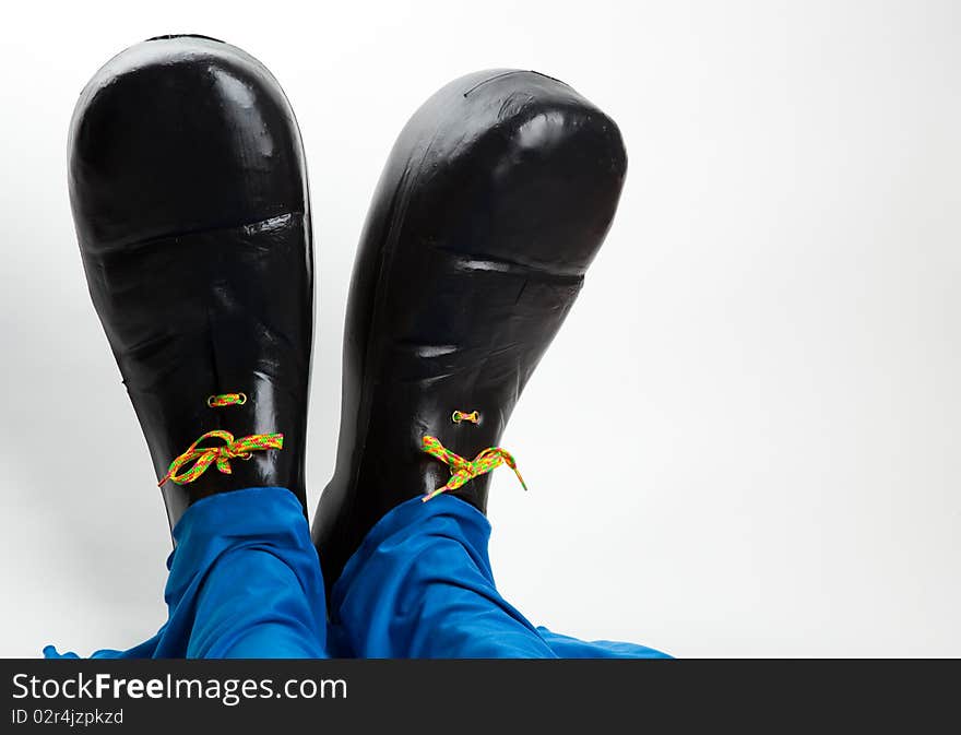 Black clown shoes and baggy blue pants against white background