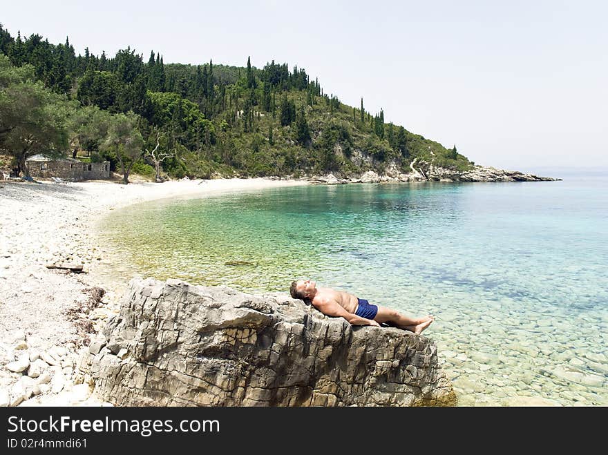 Color landscape photo of a caucasian man laying on rocks and sunbathing along a stunning beach in Paxos Greece. Color landscape photo of a caucasian man laying on rocks and sunbathing along a stunning beach in Paxos Greece.