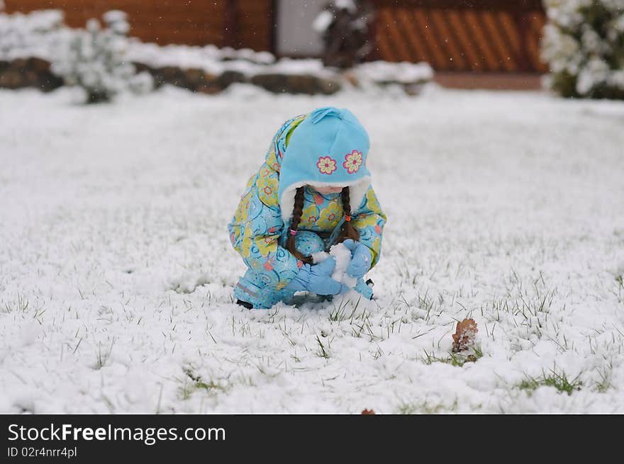 Winter toddler girl in warm  hat playing with snow