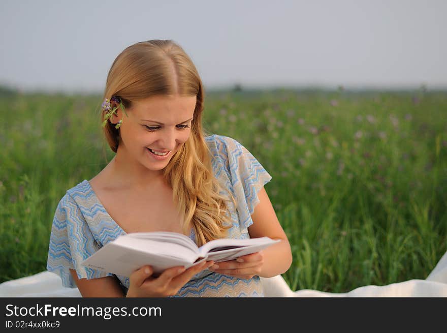 Young girl sitting on green grass and reading a book