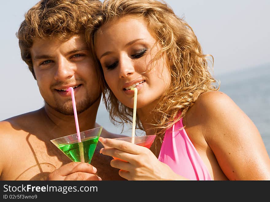 Young man and woman on the seaside with cocktails. Focus on woman. Young man and woman on the seaside with cocktails. Focus on woman