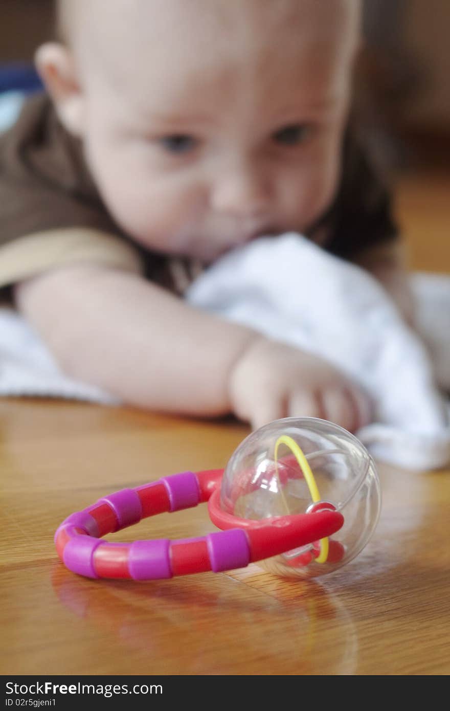 Baby boy in distance reaching for a toy rattle in the foreground. Baby boy in distance reaching for a toy rattle in the foreground