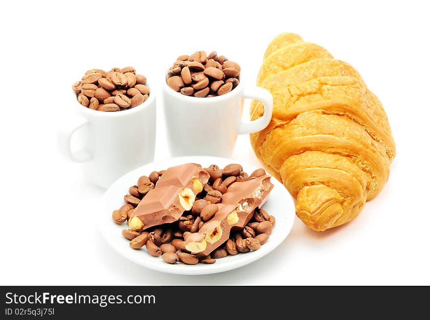 Two cups and plate filled with coffee beans and croissant isolated. Two cups and plate filled with coffee beans and croissant isolated