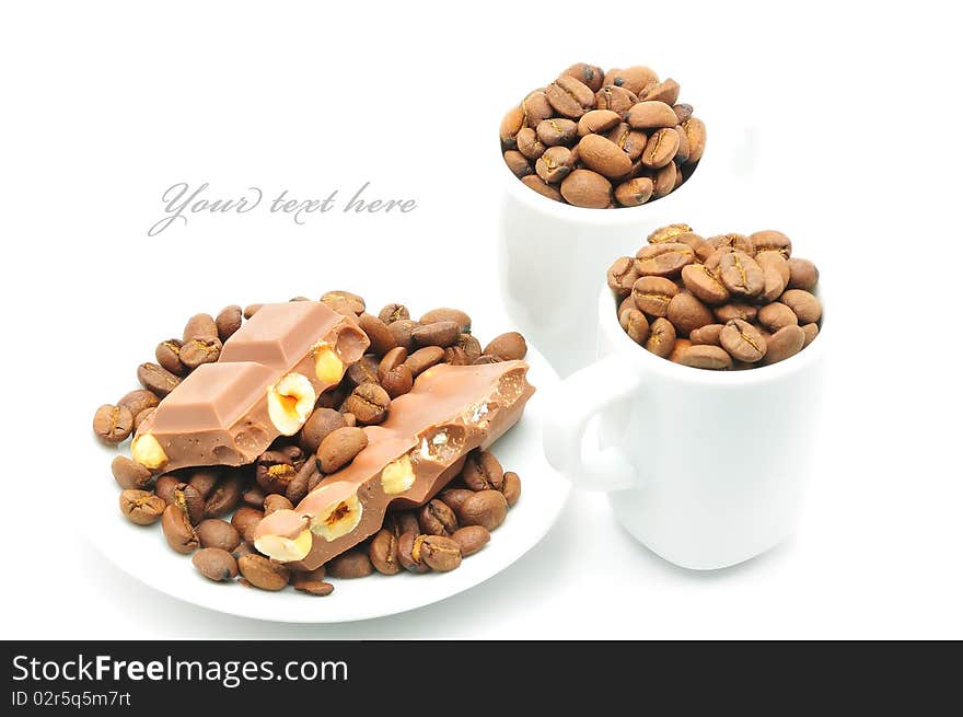 Two cups and plate filled with coffee beans and chocolate isolated. Two cups and plate filled with coffee beans and chocolate isolated