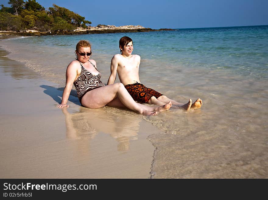 Mother and son sitting at the beautiful sandy beach and enjoying the sun and the water. Mother and son sitting at the beautiful sandy beach and enjoying the sun and the water