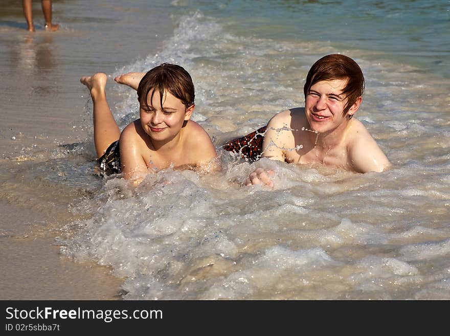 Brothers are lying at the beach  and enjoying the sun and the water