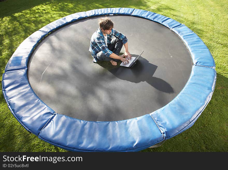 Young Man Relaxing On Trampoline With Laptop