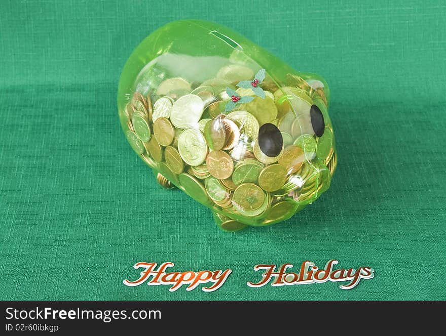 Piggy bank full of coins on a green textile with Happy Holidays. Piggy bank full of coins on a green textile with Happy Holidays