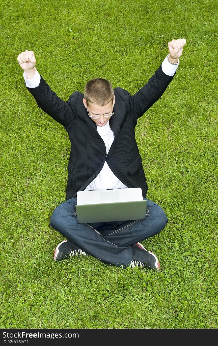 Happy businessman on the grass with laptop