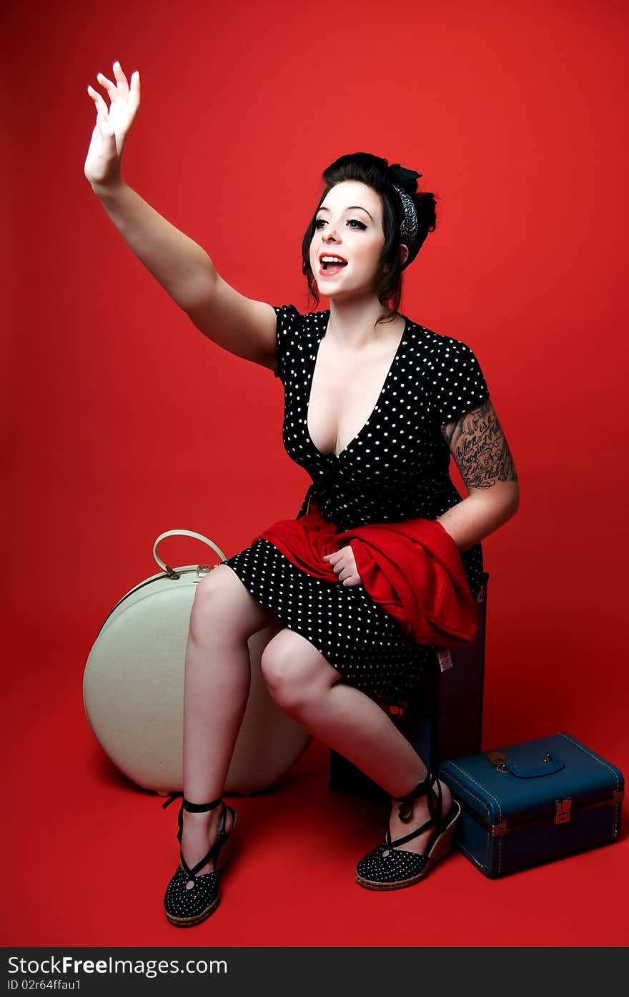 Beautiful young pinup girl sitting on luggage holding up hand. Beautiful young pinup girl sitting on luggage holding up hand