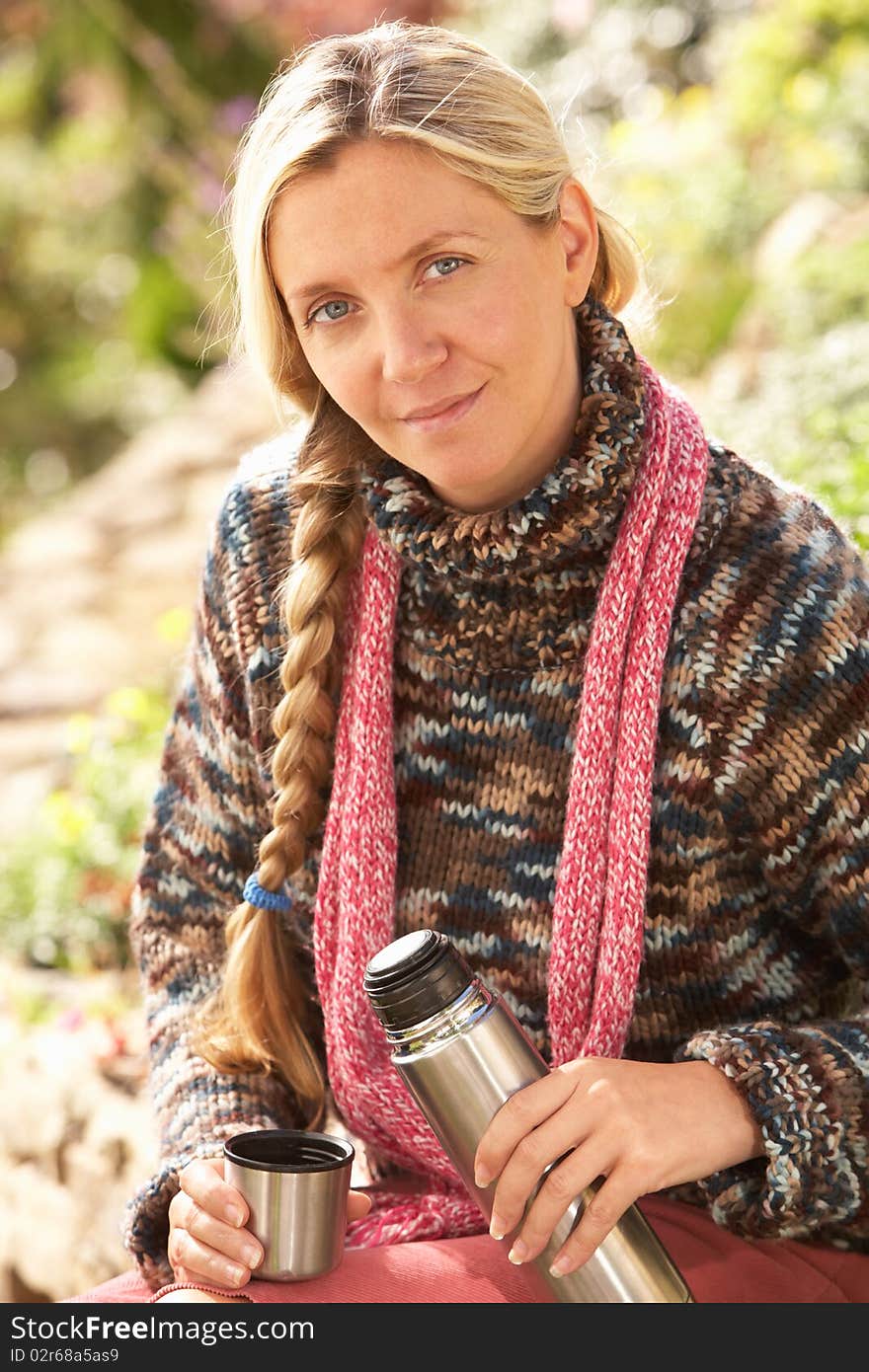 Young Woman Relaxing With Thermos Flask In Autumn Landscape