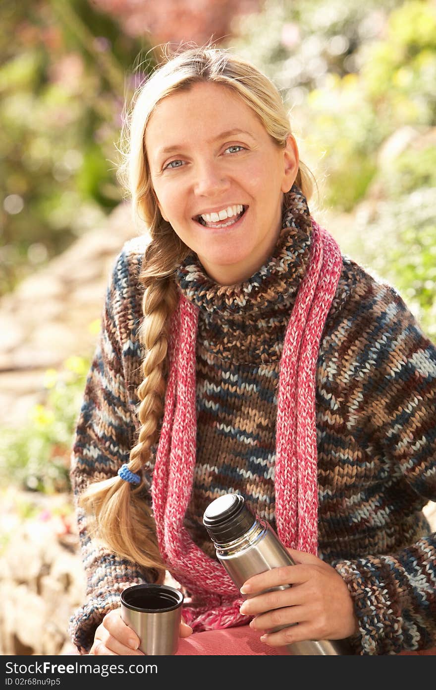 Young Woman Relaxing With Thermos Flask In Autumn Landscape