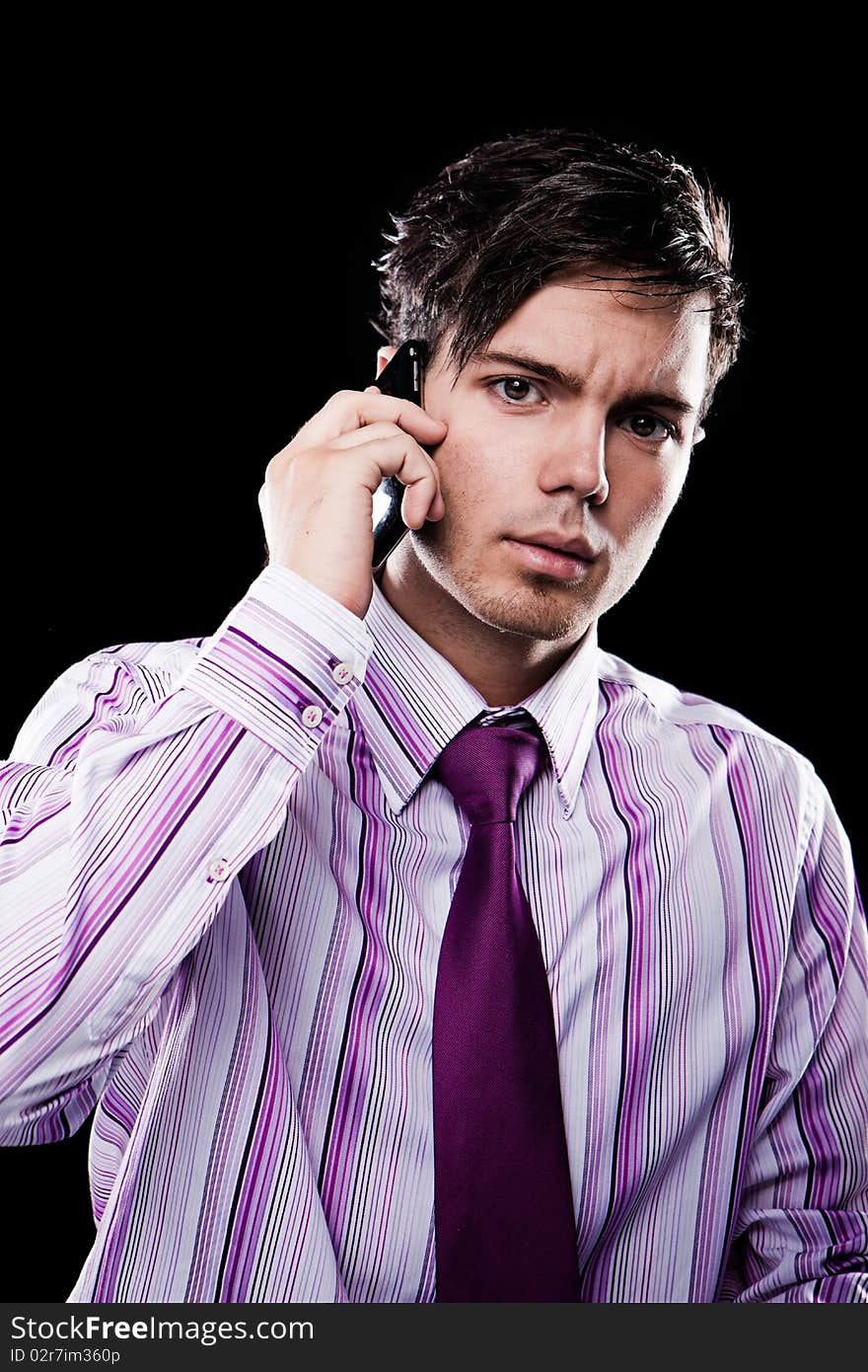 Portrait of a handsome young business man speaking on the mobile isolated on black background