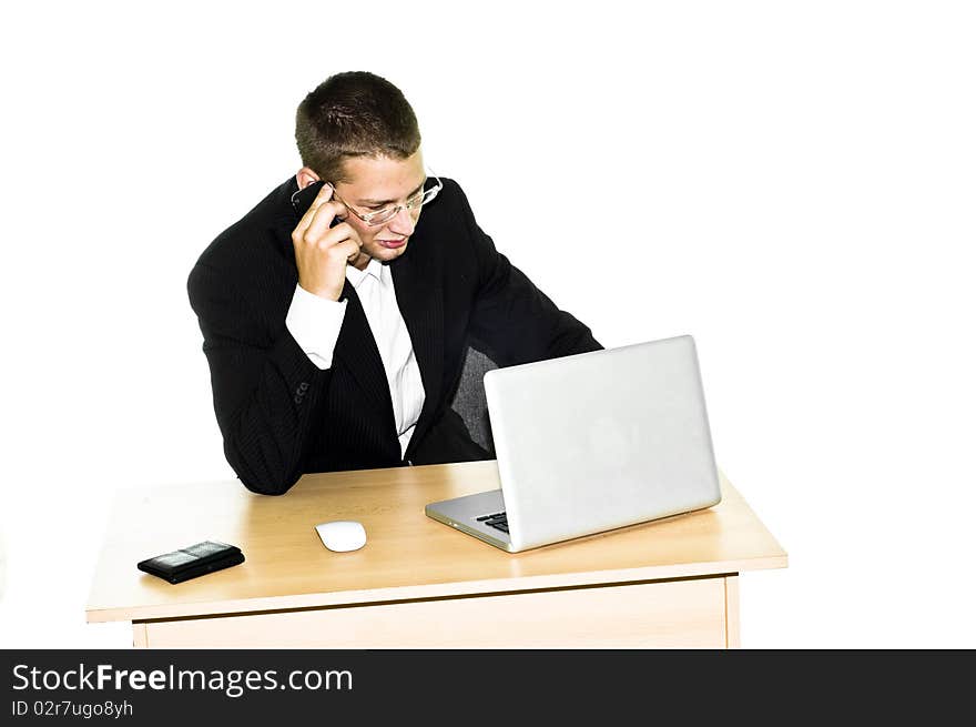 Young businessman working on desk with laptop, mouse and wallet, talking on mobile phone. Young businessman working on desk with laptop, mouse and wallet, talking on mobile phone