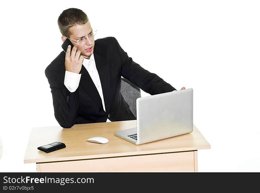 Young businessman irritated while working in office, looking at laptop and talking on mobile phone. Young businessman irritated while working in office, looking at laptop and talking on mobile phone