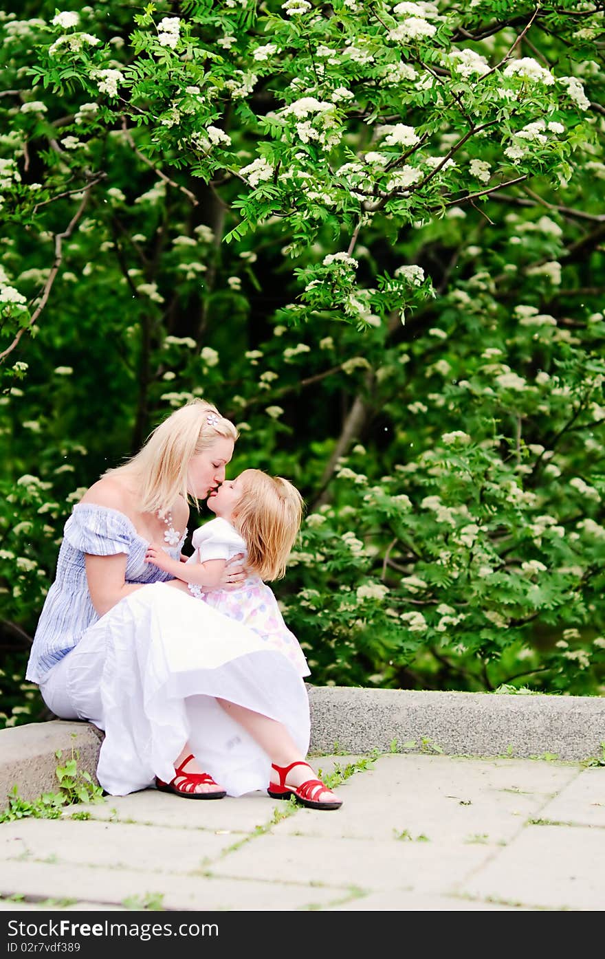 Beautiful blond woman and her baby daughter kissing in blooming garden. Beautiful blond woman and her baby daughter kissing in blooming garden