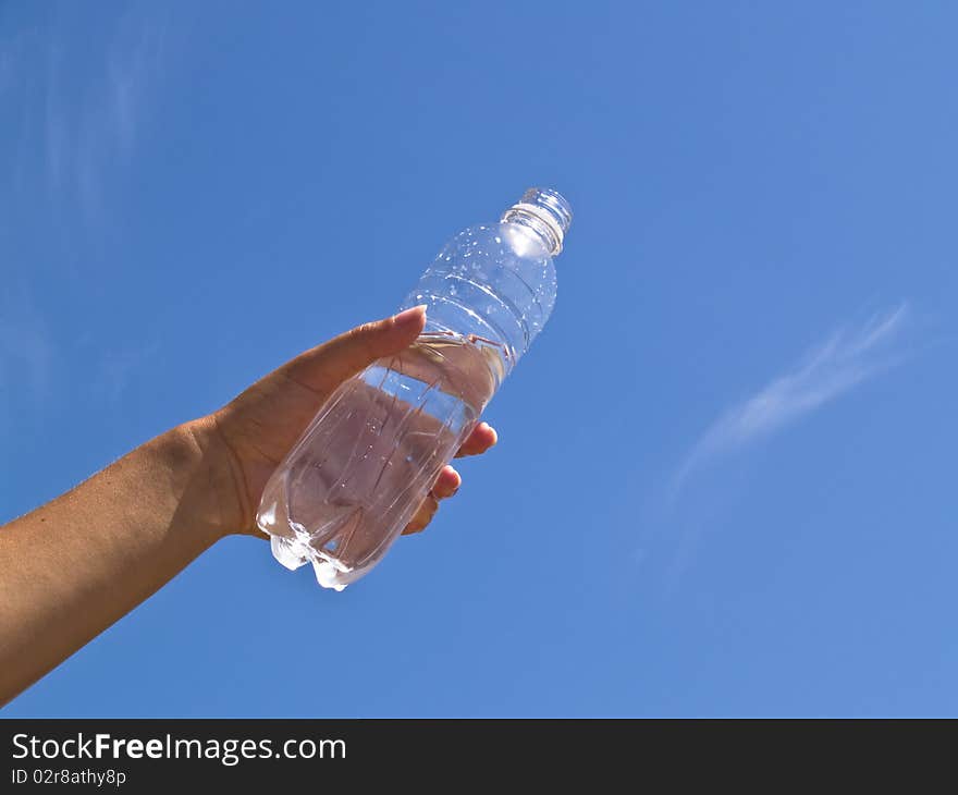 Hand holding bottle of water on the blue sky background