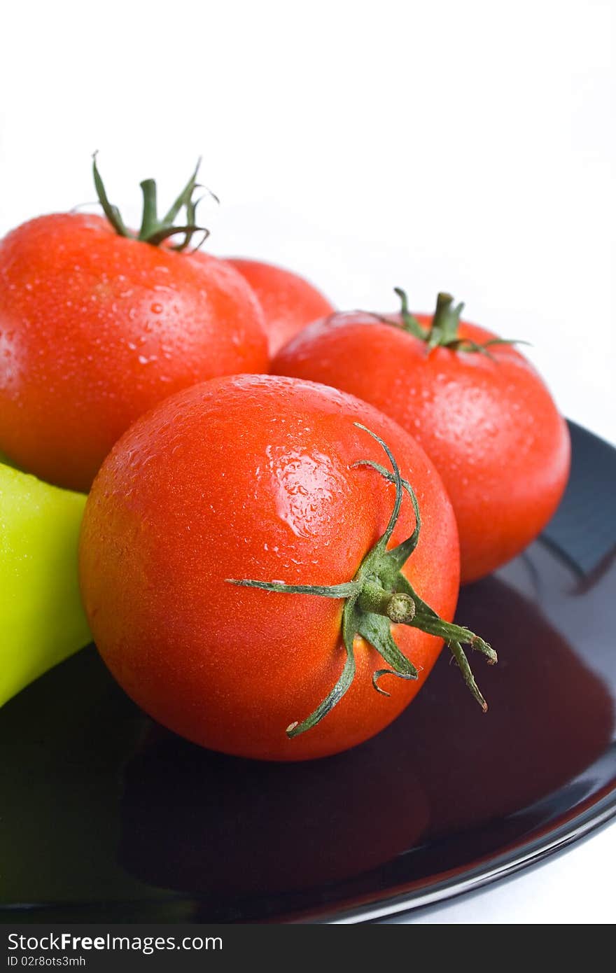 Fresh tomatoes washed and placed in a black ceramic plate isolated on white background