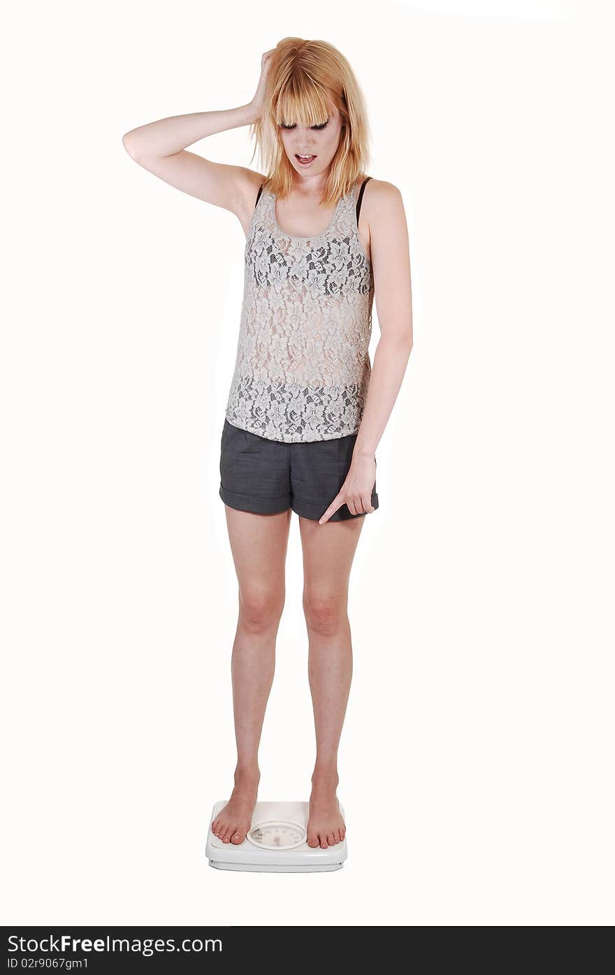 A young woman is very sad, standing on a scale and find out she gains some wait, in shorts and a lace top on white background. A young woman is very sad, standing on a scale and find out she gains some wait, in shorts and a lace top on white background.