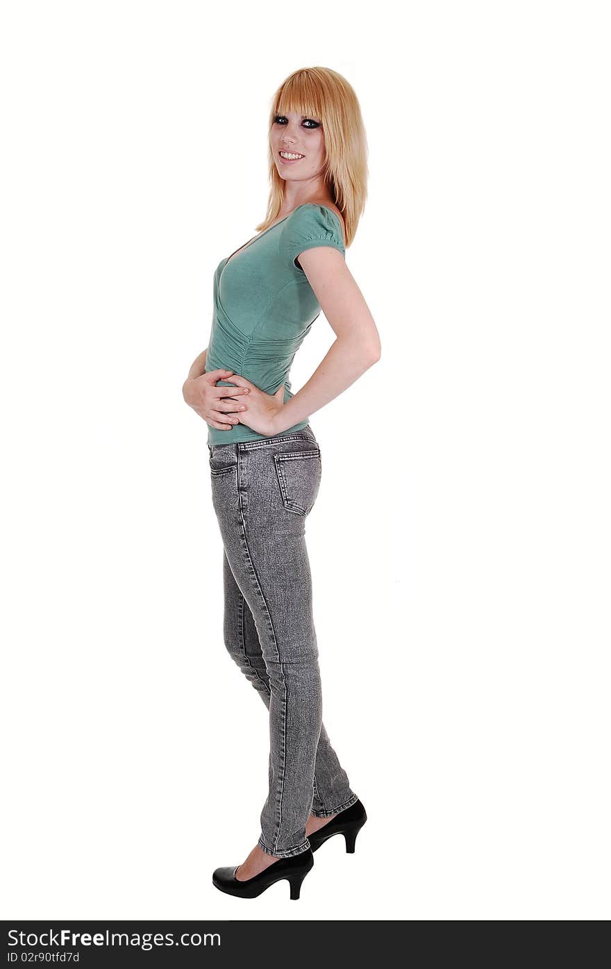 A beautiful tall and slim woman in gray jeans and green sweater standing in the studio in profile and smiling into the camera, on white background. A beautiful tall and slim woman in gray jeans and green sweater standing in the studio in profile and smiling into the camera, on white background.