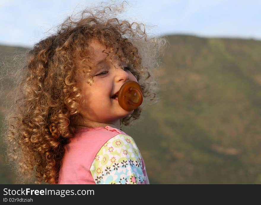 Closeup of little angelic curly laughing girl with soother. Closeup of little angelic curly laughing girl with soother