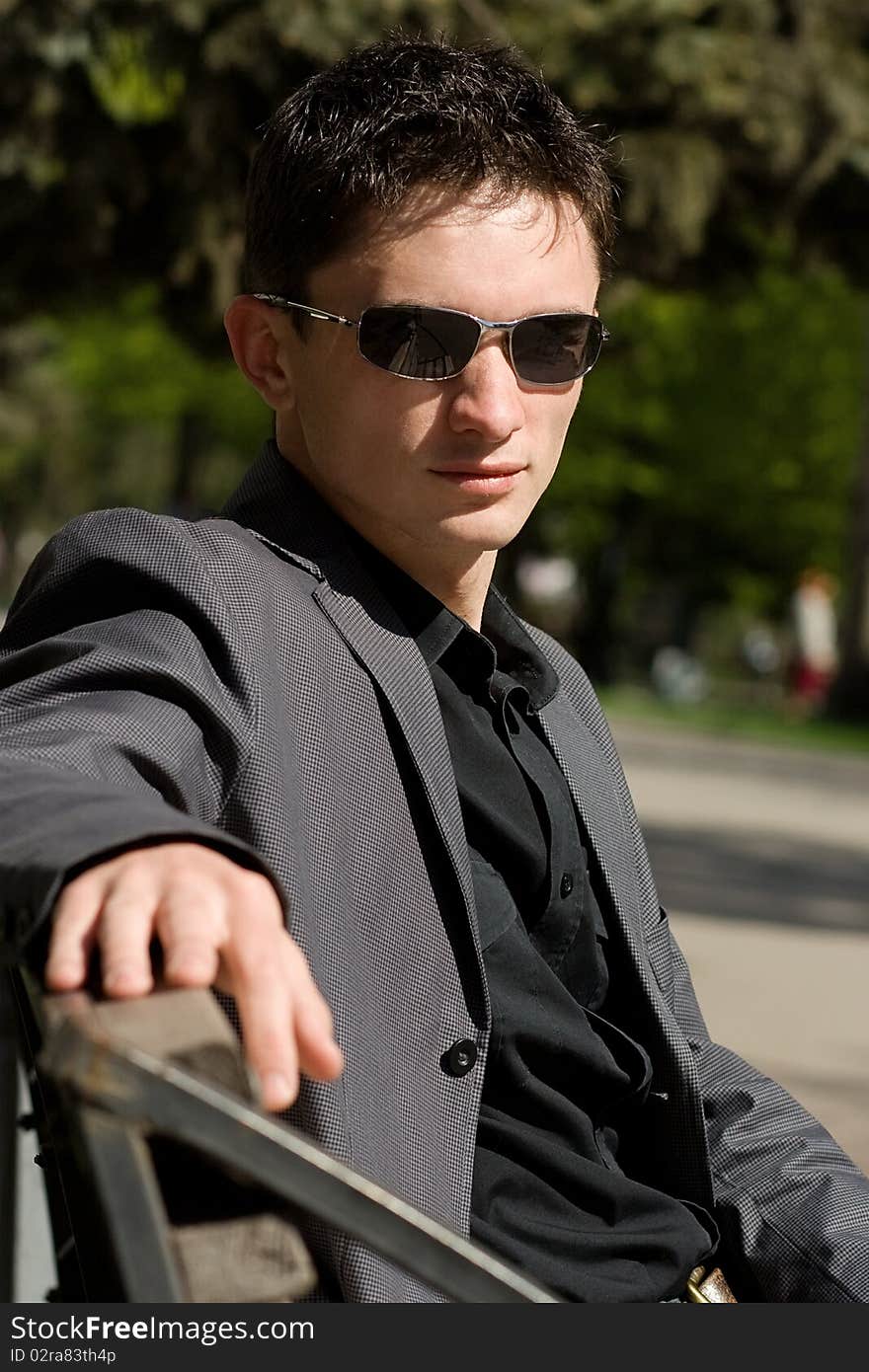 Man in sunglasses and jacket sitting on a bench in the middle of a day. Man in sunglasses and jacket sitting on a bench in the middle of a day