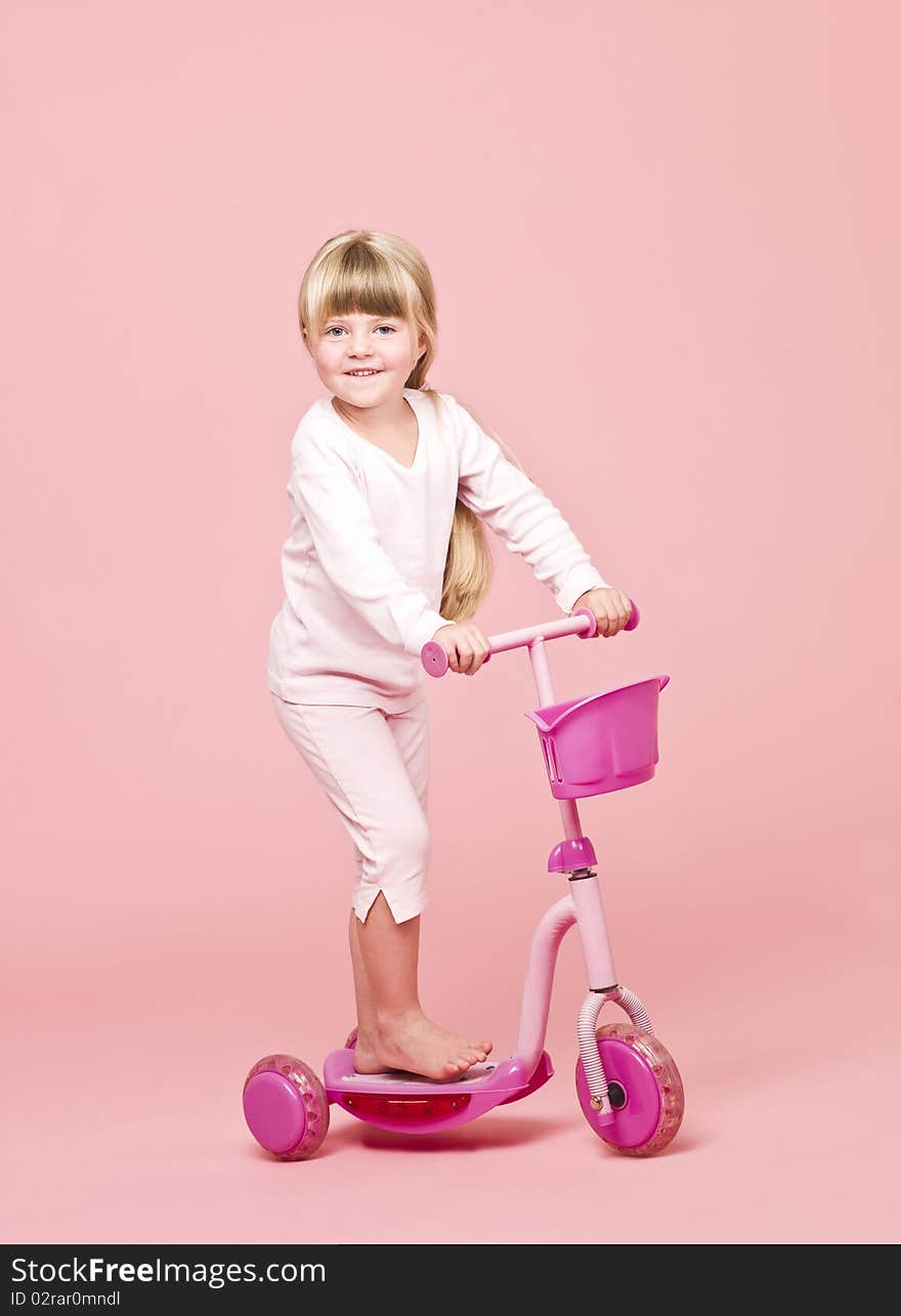 Young girl with a scooter towards pink background