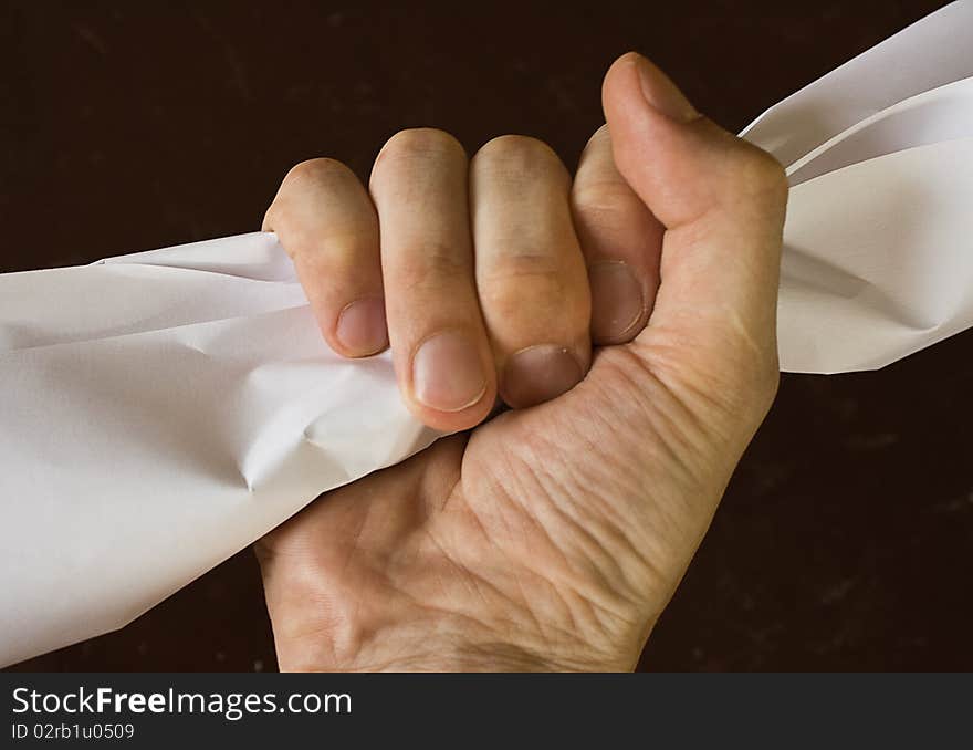 The hand squeezes a piece of paper against a dark background. The hand squeezes a piece of paper against a dark background