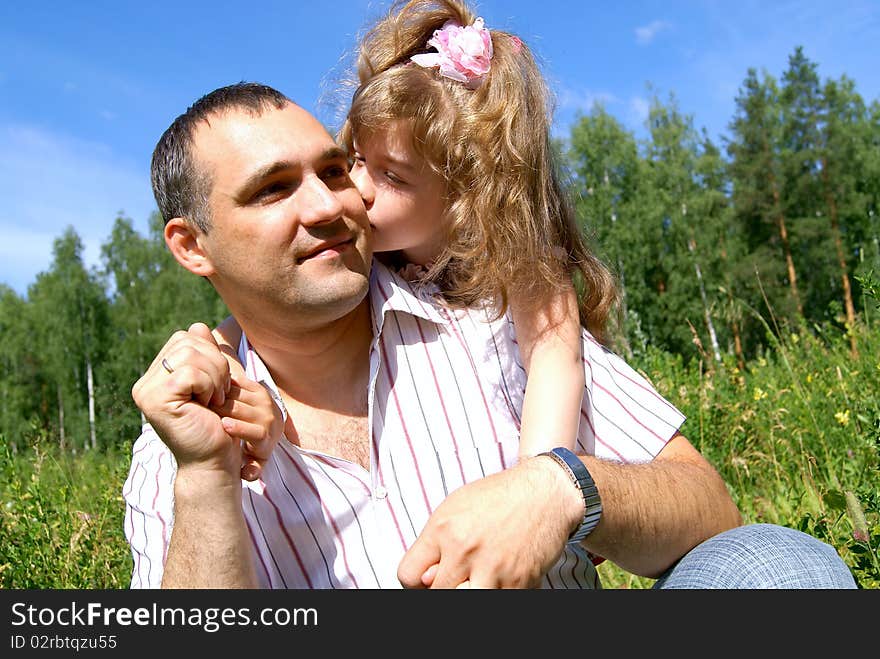 The daughter embraces the daddy and kisses him on a cheek in the summer on the nature. The daughter embraces the daddy and kisses him on a cheek in the summer on the nature