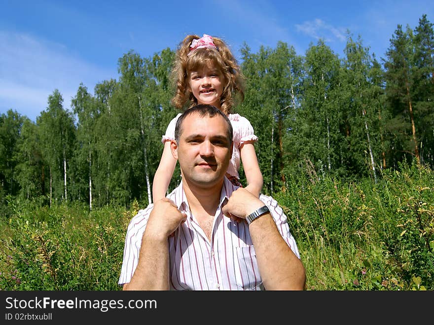 In the summer against the sky, a green grass and trees the smiling daughter embraces the daddy. In the summer against the sky, a green grass and trees the smiling daughter embraces the daddy